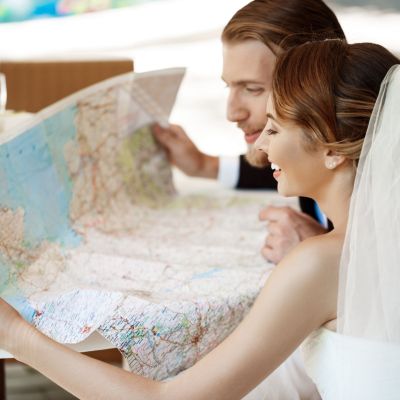 Young beautiful newlyweds smiling, choosing honeymoon trip, looking at map.